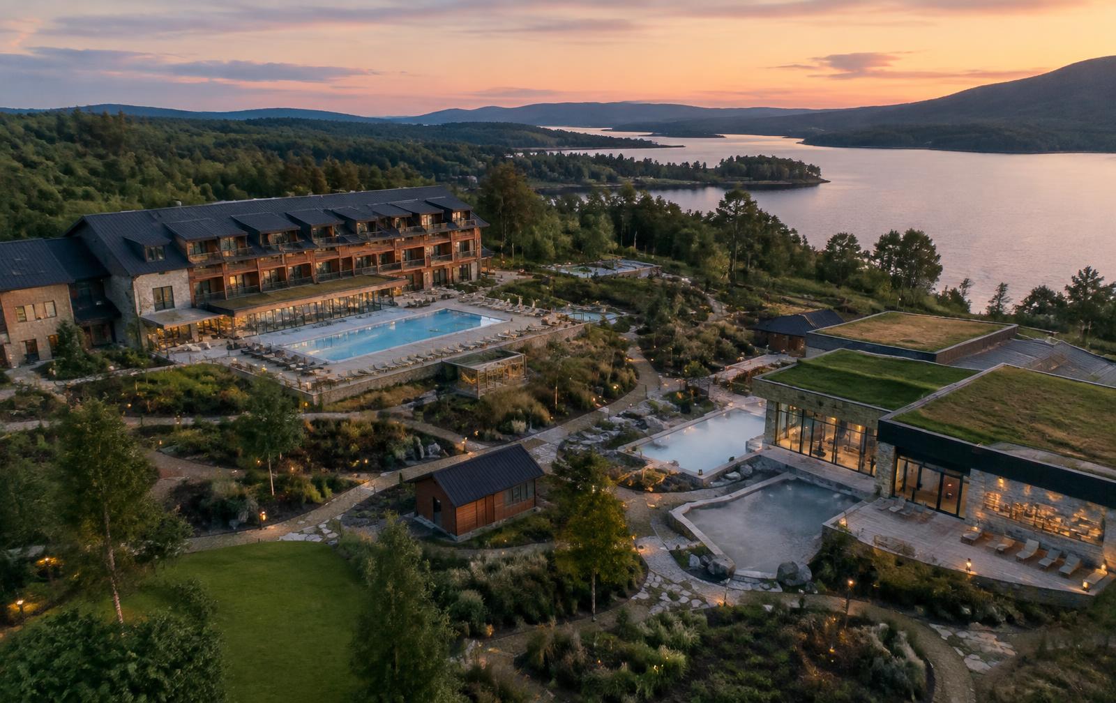 A wellness destination with pools and gardens by a lake at dusk