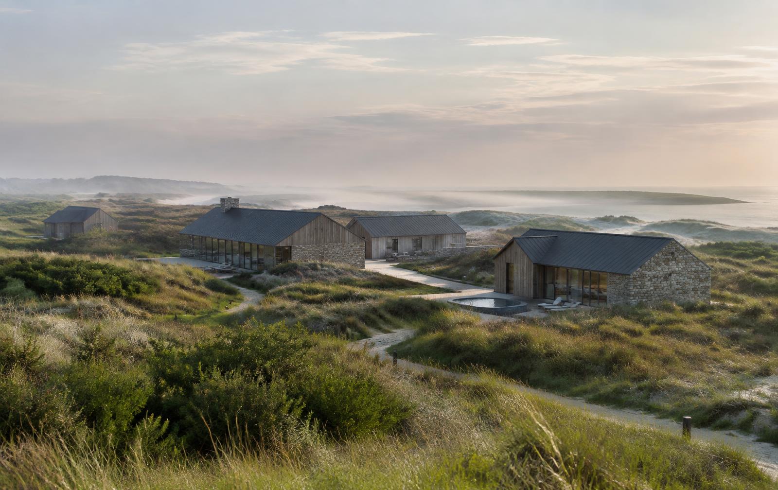 A secluded retreat of timber and stone houses among coastal dunes in morning mist